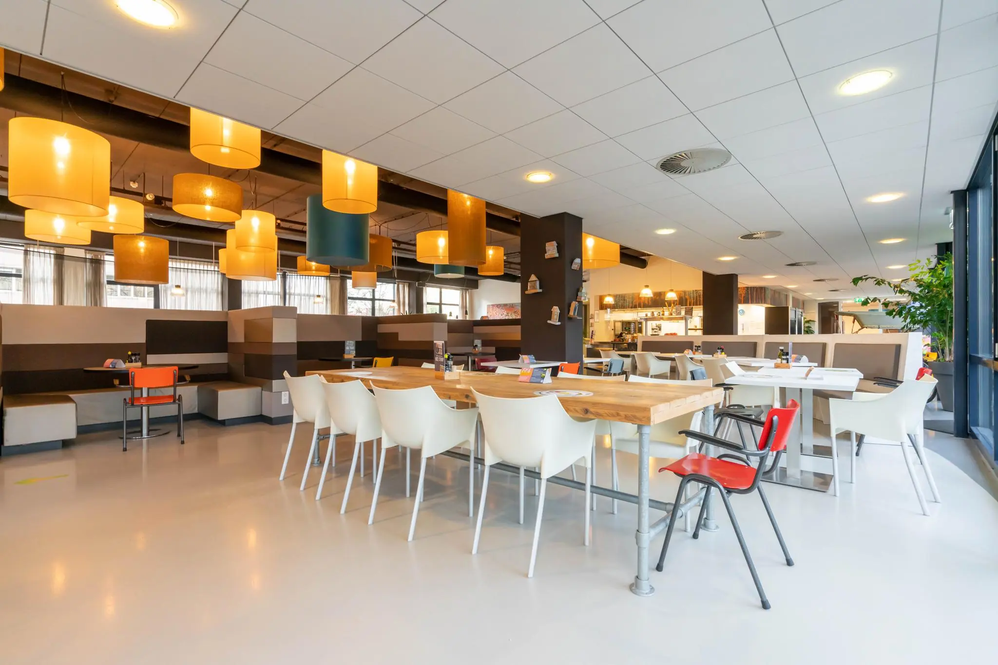 Moderne, sfeervol verlichte kantineruimte aan de De Bruyn Kopsstraat met houten tafels, witte stoelen en kleurrijke lampenkappen.